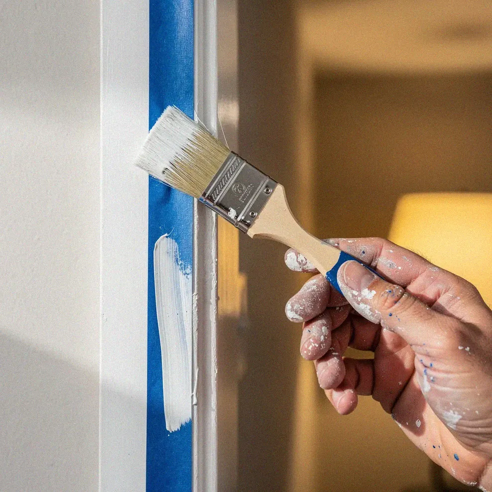 Painter cutting in white trim paint along a wall edge with an angled brush